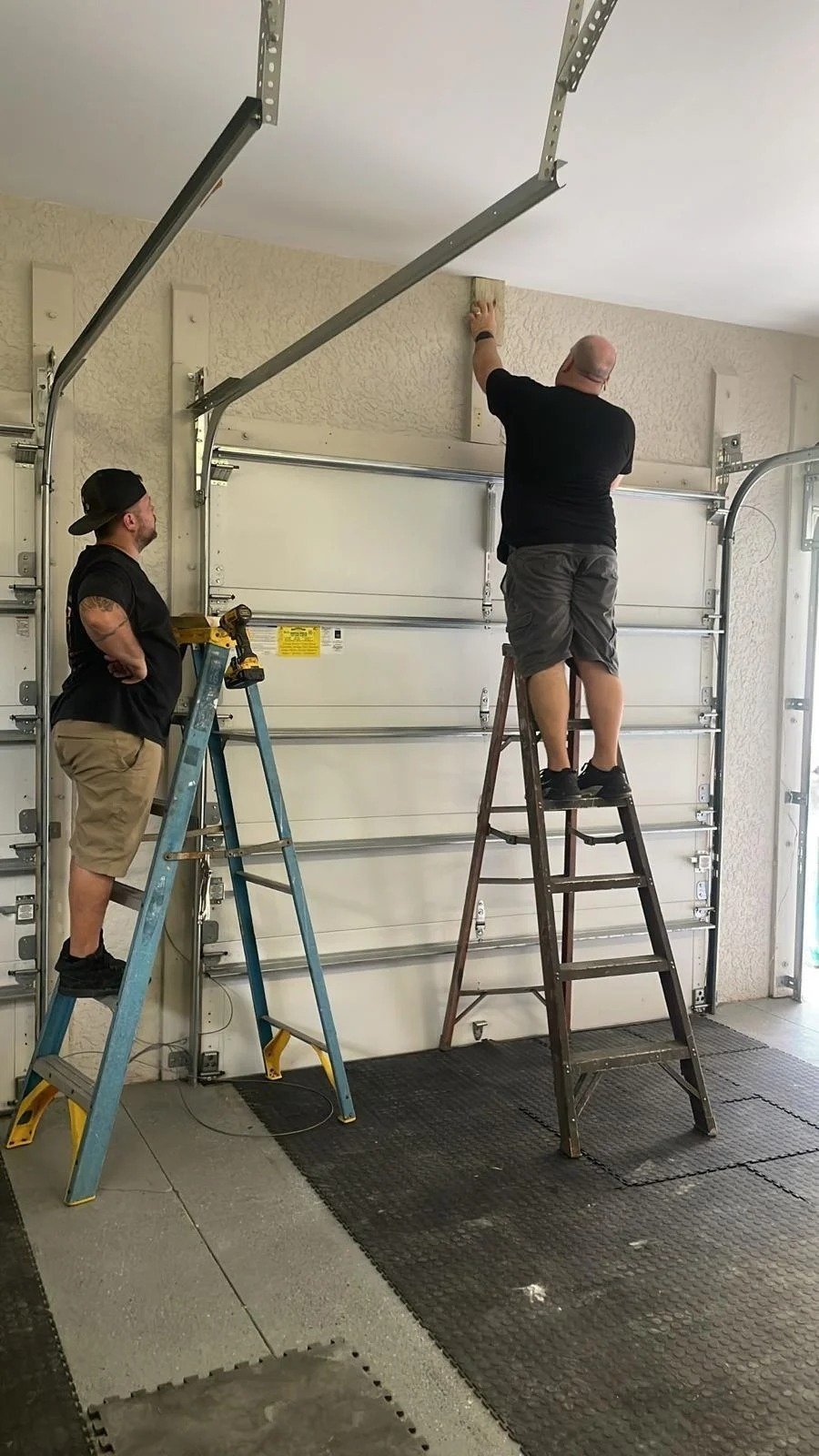 Two people on ladders working at the overhead rails of a garage door