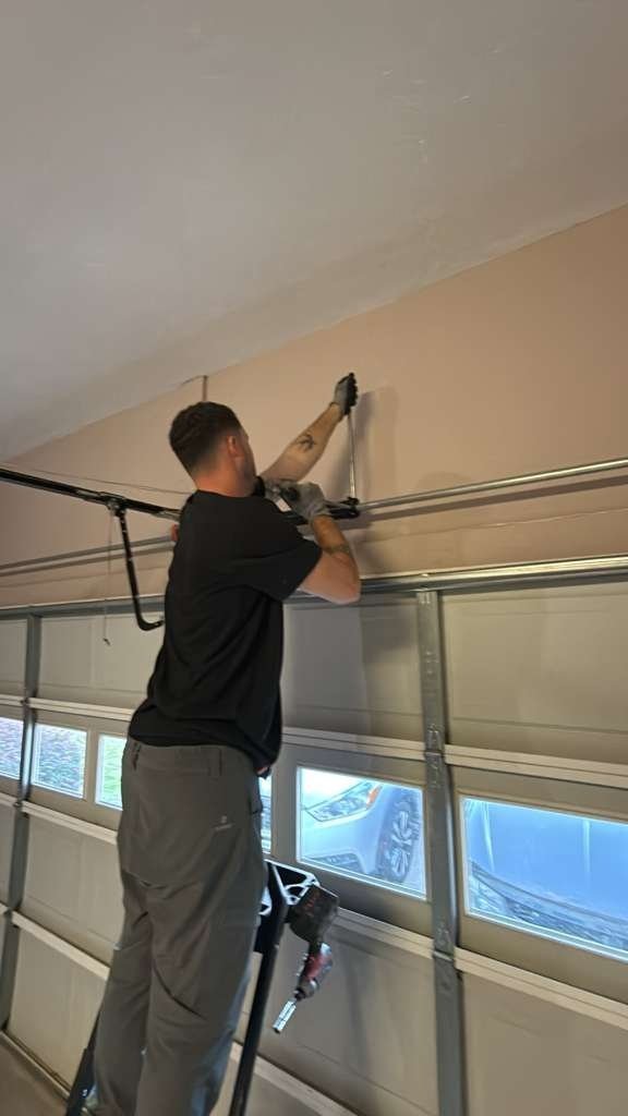 Technician reaching up to the overhead rail above a garage door with a row of small windows