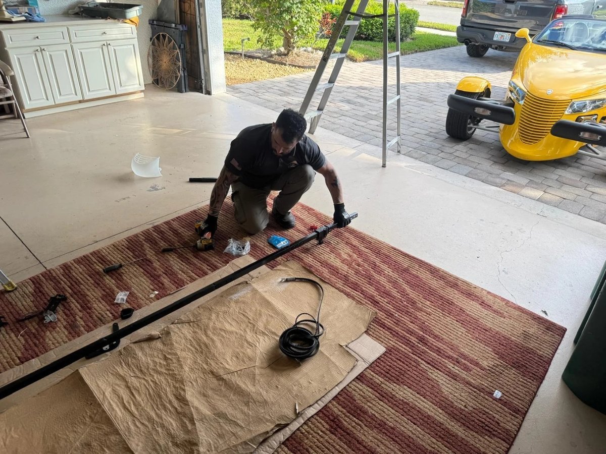 Technician laying a garage door track section on a rug-covered garage floor