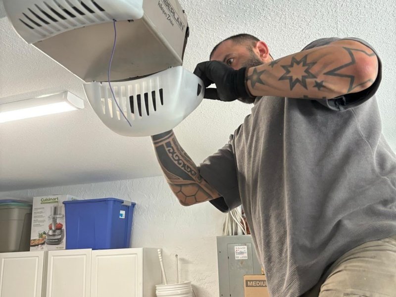 A technician in gloves holding the cover of a ceiling-mounted garage door opener