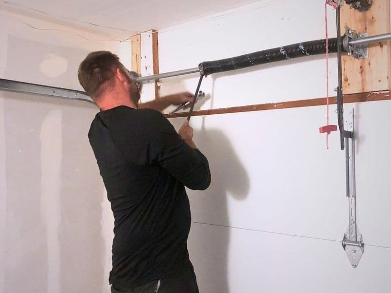 Technician using a winding bar at torsion hardware above a closed door